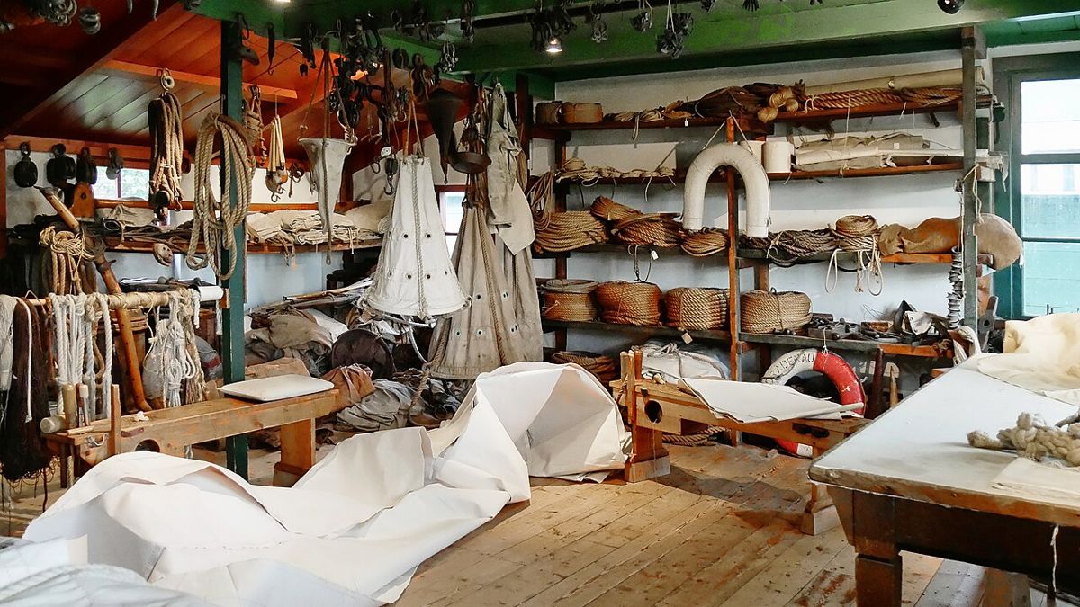 Atelier de voilier traditionnel : toiles étalées au sol, cordages et outils de couture